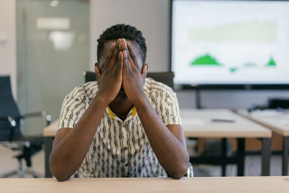A stressed employee covering face in a modern office, depicting work pressure.