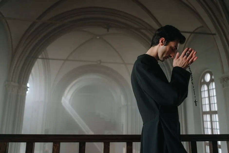 Side view of a priest praying with a rosary in a historic church setting.