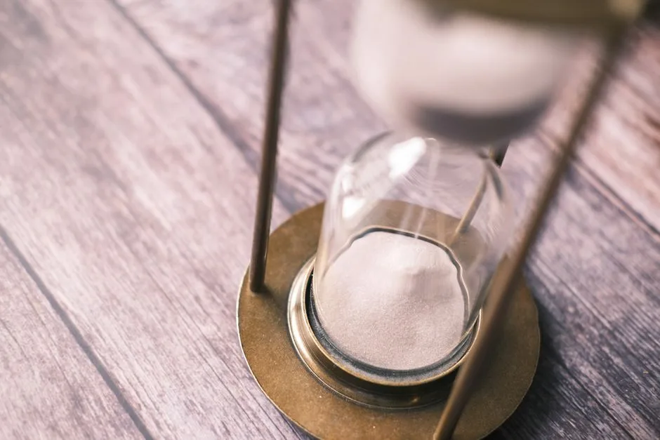 Close-up of a vintage hourglass with sand flowing on a wooden background.