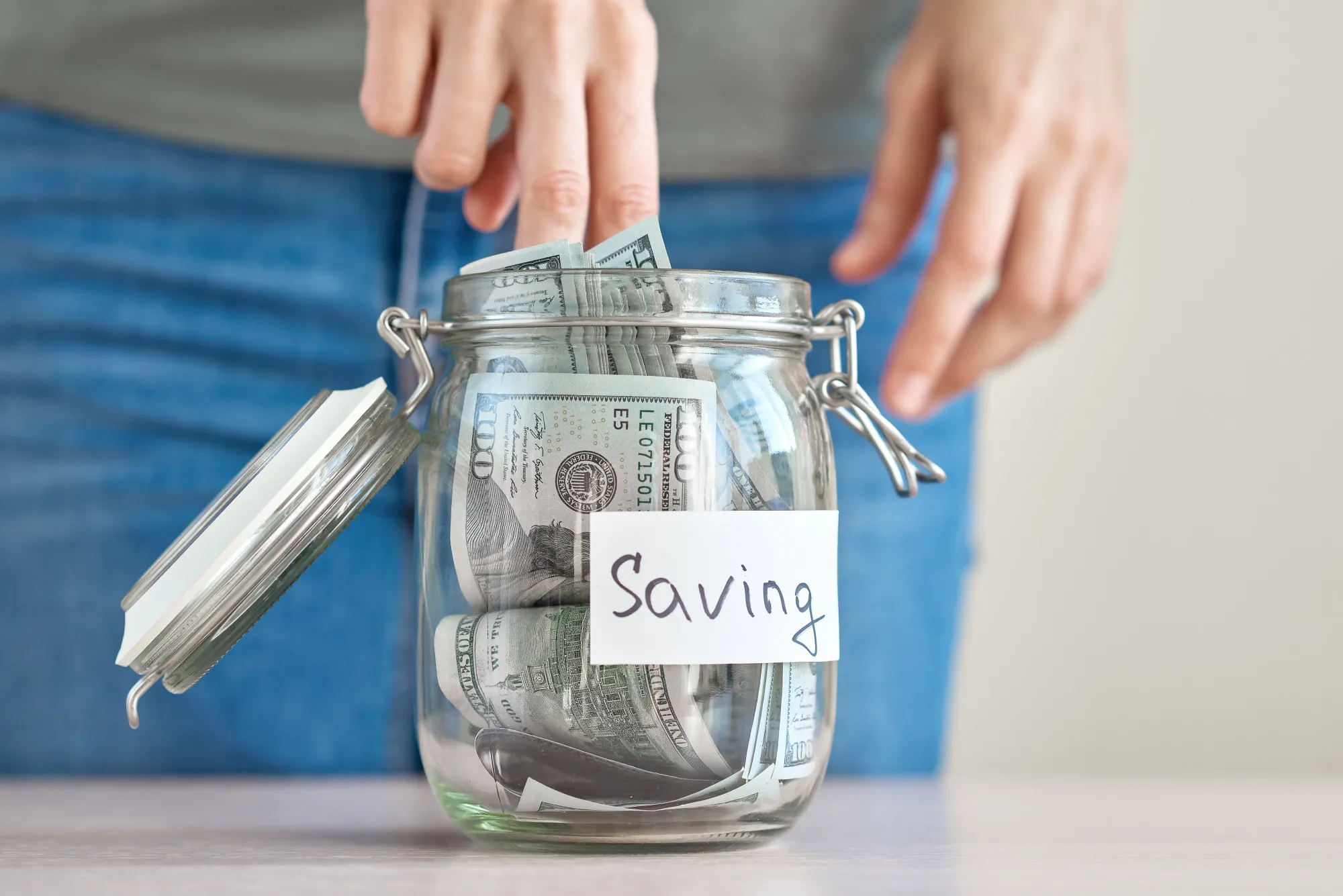 Woman hand holding us dollar bill and putting in a glass jar with inscription saving. Saving money and home budget concept
