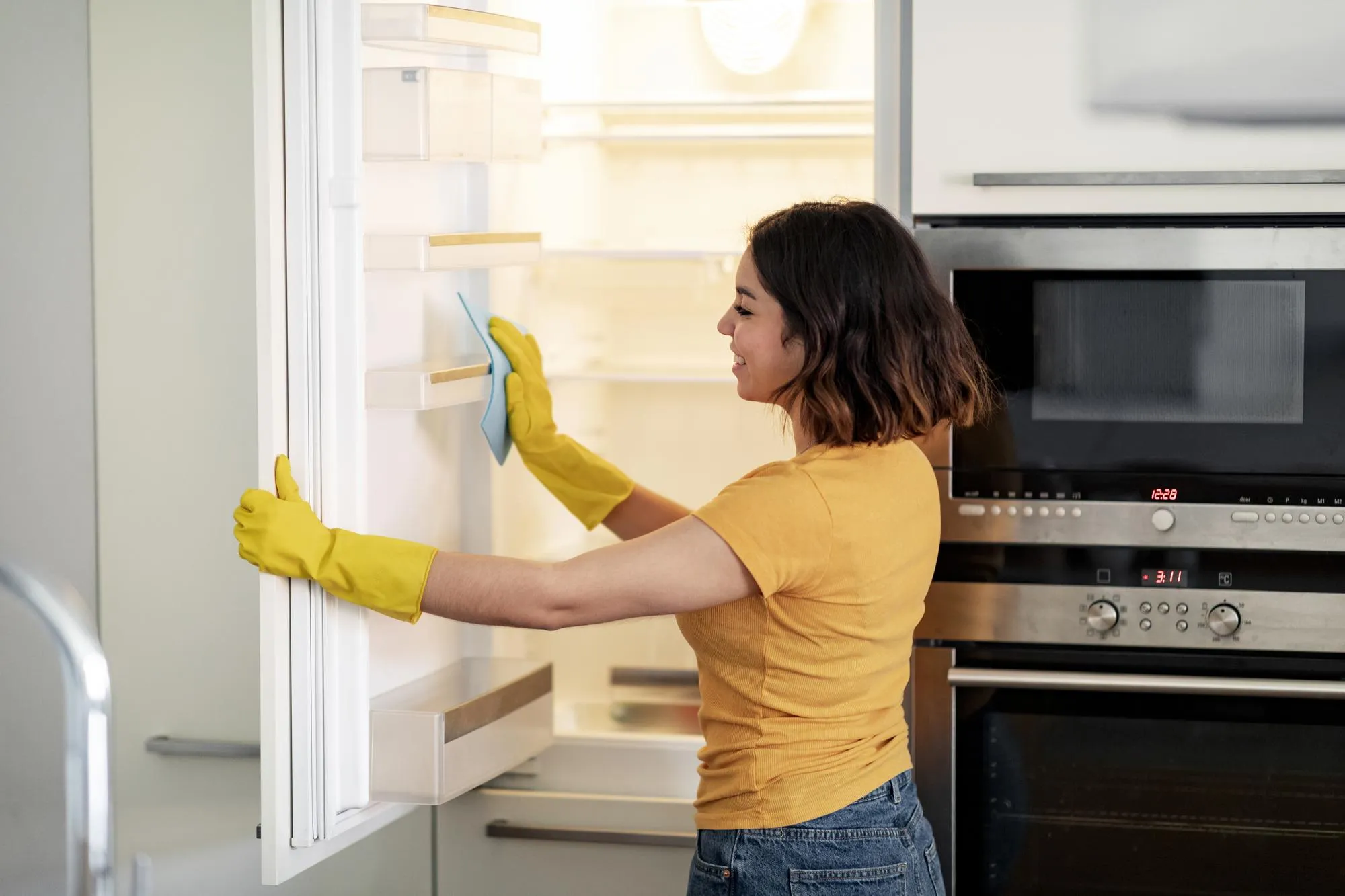 Young Arab Female Using Rag For Cleaning Empty Fridge In Kitchen