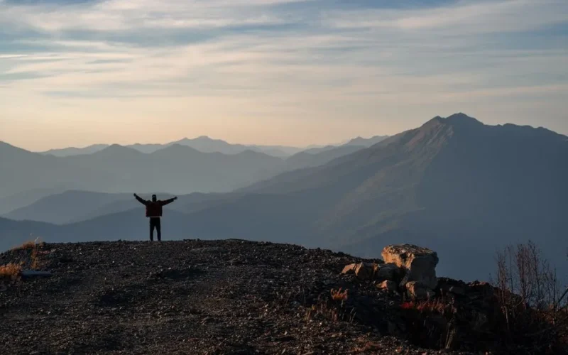 A person stands triumphantly on a mountain peak, silhouetted against a stunning sunrise.