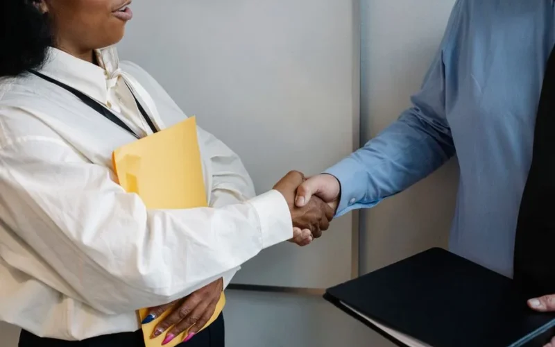 Crop unrecognizable multiethnic colleagues standing with documents and shaking hands while greeting each other in office