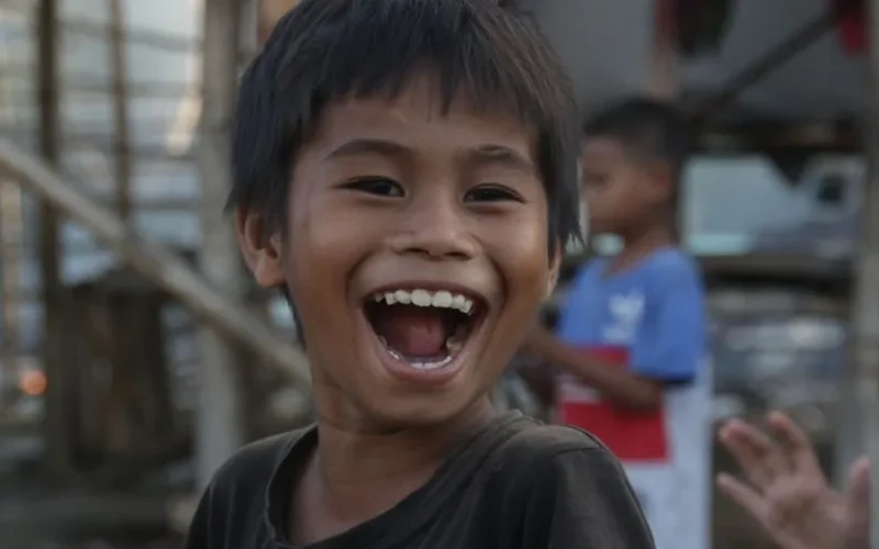 A cheerful Asian boy with a big smile outdoors, expressing happiness and joy.