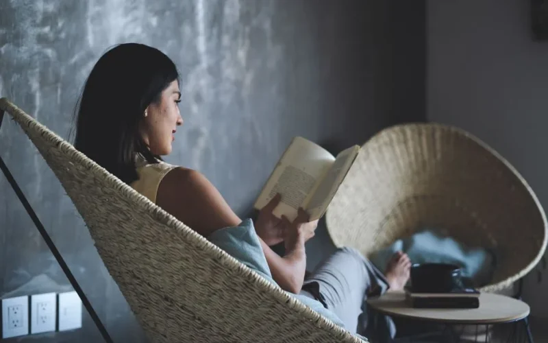 A woman enjoys a leisure moment reading a book in a cozy indoor setting.