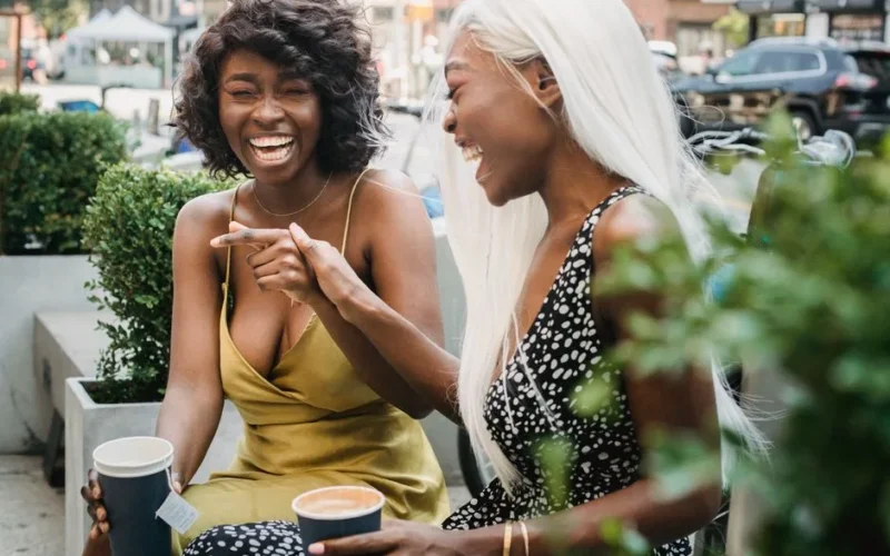 Two friends laughing together while enjoying hot drinks outside, embodying joy and companionship.