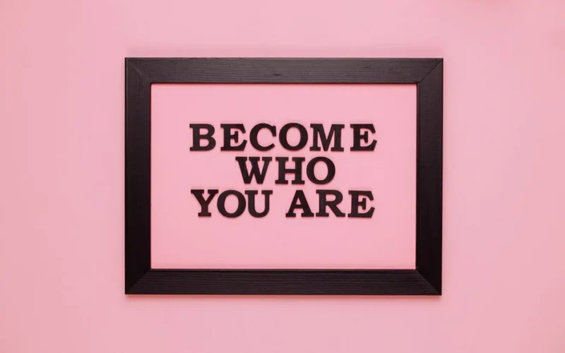 Inspiring quote 'Become Who You Are' framed on a vibrant pink wall, perfect for encouragement.