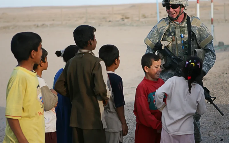 Staff Sgt. Kevin M. OâBrien, infantryman, bridges the language barrier and shares a laugh with a local Iraqi children in a village near Camp Taqaddum, Iraq, March 12th, 2006. OâBrien, 37, of Monticello, Ill., and the other soldiers from 2nd Battalion, 130th Infantry Regiment, performed a multi-faceted mission during the daylong operation as they carried out weapons cache sweeps, investigated possible improvised explosive devices and conducted route clearance operations. The Illinois-based National Guard took a few moments throughout the day to assist Iraqi villagers in the area, handing out supplies and spending time with the local children. The soldiers were grateful it wasnât business as usual and could do something a little light hearted. Whether itâs handing out candy or searching for IEDs, the soldiers are proud of what they are doing in Iraq, said Sgt. 1st Class Timothy J. Atteberry, platoon sergeant. âœThe individual, personal satisfaction of helping another human being really comes from these kinds of humanitarian-aid type missions,â said Atteberry, a 38-year-old native of Champagne, Ill. The soldiersâ€™ primary mission is to provide base security for the Marines and sailors of the forward-deployed 1st Marine Logistics Group. The 4,200 joint-service members of 1st MLG are part of the 25,000 Marines, airmen, solders and sailors of the 1st Marine Expeditionary Forceâ€™s forward deployed element. The 1st MLGâ€™s mission is to provide sustained logistics support to I MEF and Iraqi security forces operating in the Al Anbar province of Iraq. First MLG will also support the development of the Iraqi Security Forcesâ€™ logistic capabilities in order to enable independent ISF led counter insurgency operations.