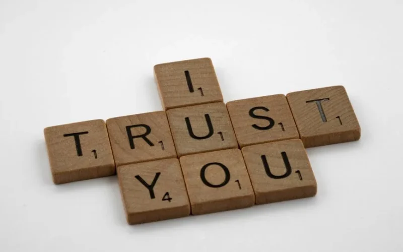 Close-up of Scrabble tiles arranged to spell 'I Trust You' on a white background, symbolizing trust.