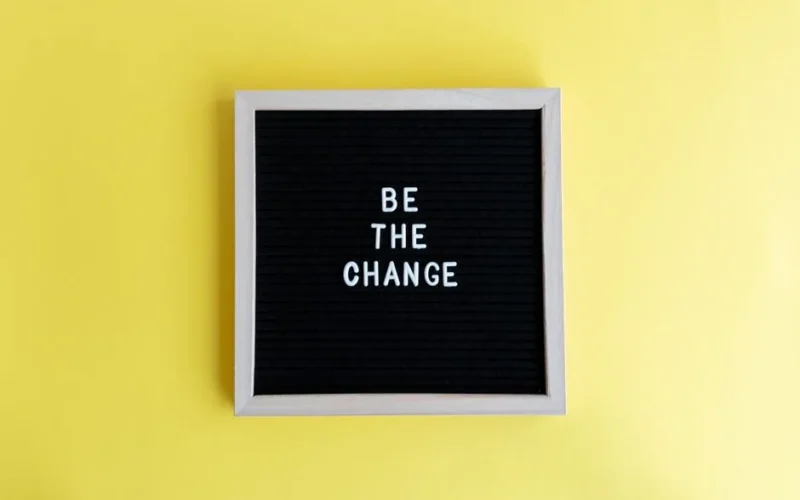 Minimalist letter board with 'Be The Change' quote on a vibrant yellow background.