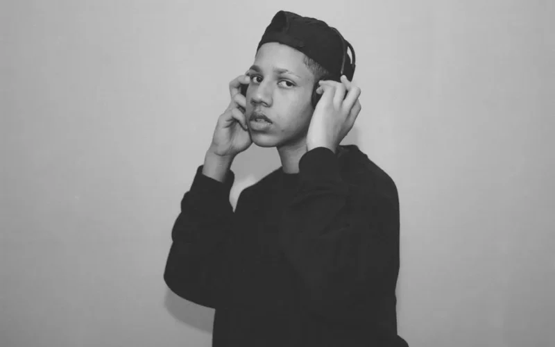 Black and white of pensive young ethnic male millennial listening to music in headphones and looking at camera