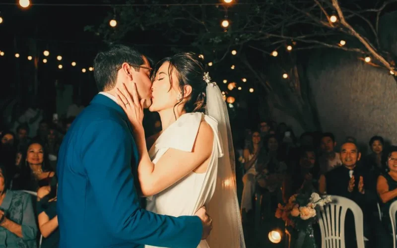 Newlywed couple sharing a romantic kiss under enchanting outdoor string lights.