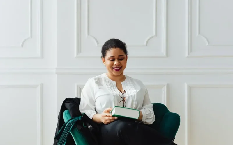 Smiling African American woman enjoying a book indoors, in a modern setting.