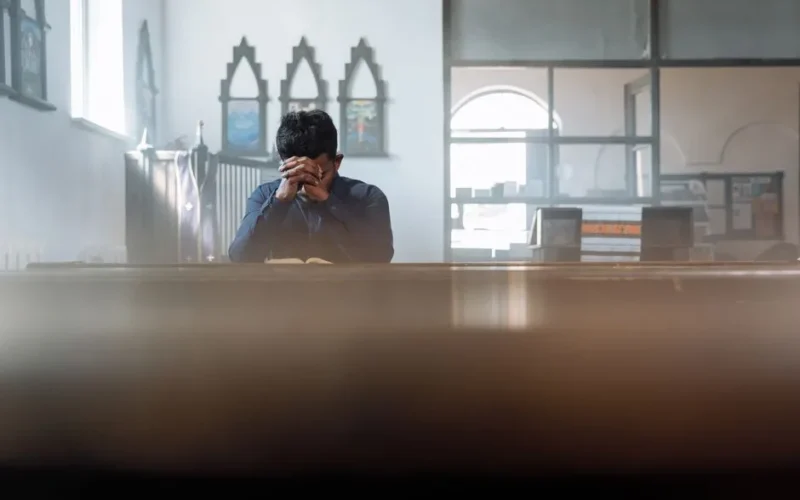 A man in prayer in a sunlit room, reflecting spirituality and peace.