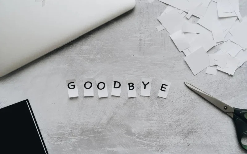 Artistic flat lay featuring the word 'GOODBYE' crafted from paper cutouts with scissors and a laptop.