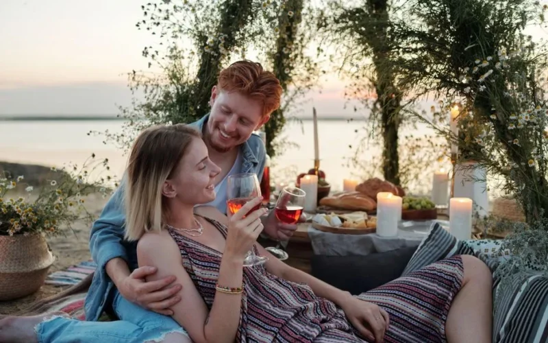 Couple enjoying a romantic outdoor picnic with wine and candles, creating a perfect evening atmosphere.