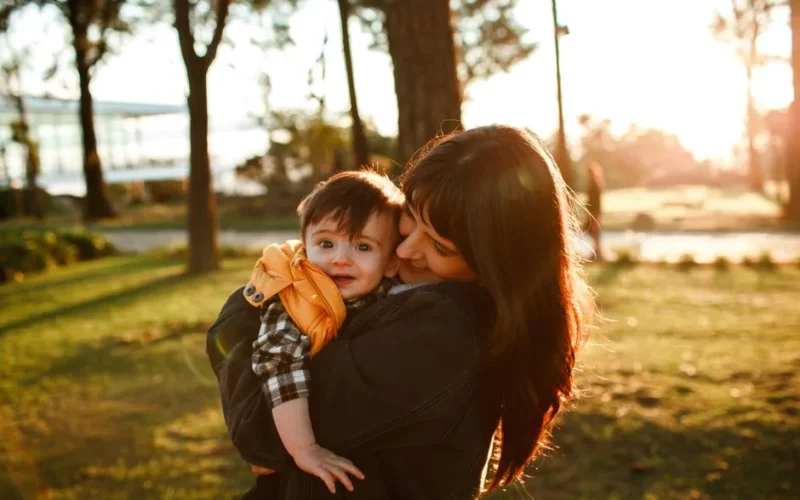 A mother embraces her child outdoors during a warm sunset, capturing love and bonding.