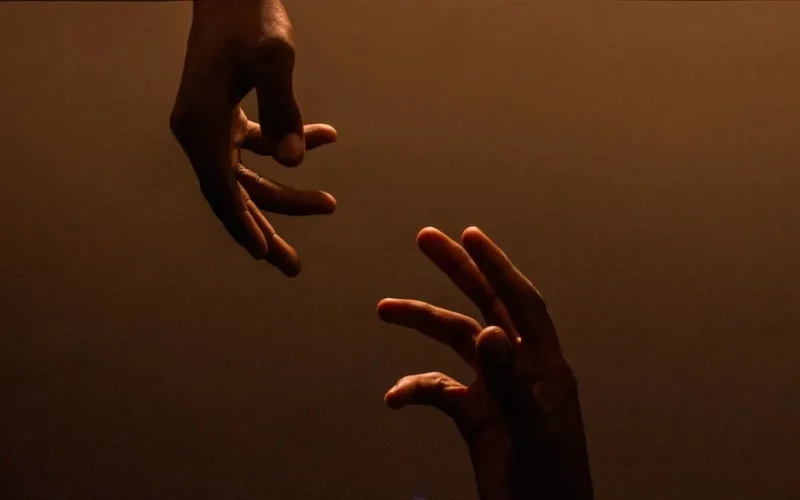 Two hands reaching towards each other against a dark, warm background, symbolizing connection.