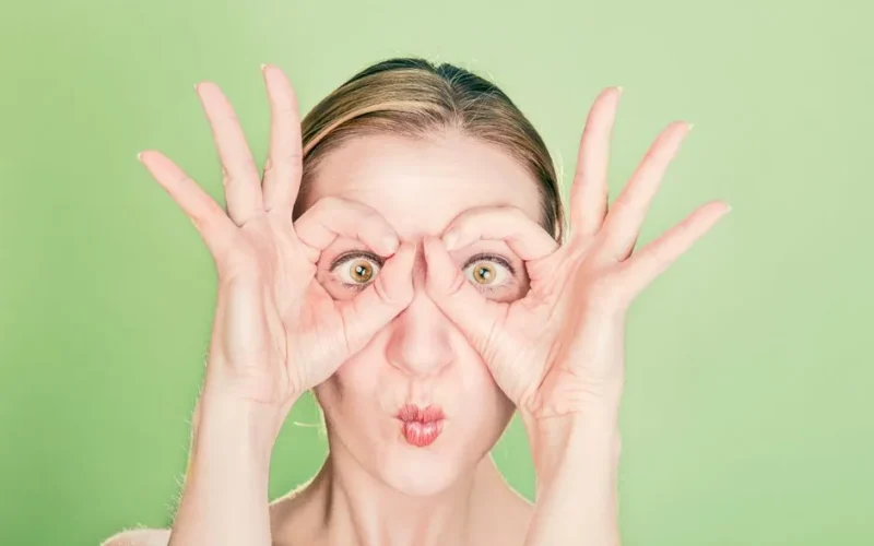 A woman creates a funny face with her hands and eyes against a green background. Perfect for whimsical themes.
