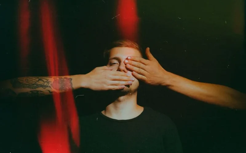 Artistic portrait of a man with hands covering eyes and mouth, creating a dramatic effect.
