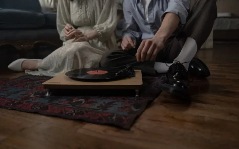 Couple sits on floor by a turntable, enjoying nostalgic vinyl music indoors.