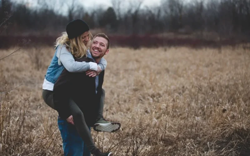 A happy couple enjoys a playful moment in a field during the day, symbolizing love and joy.