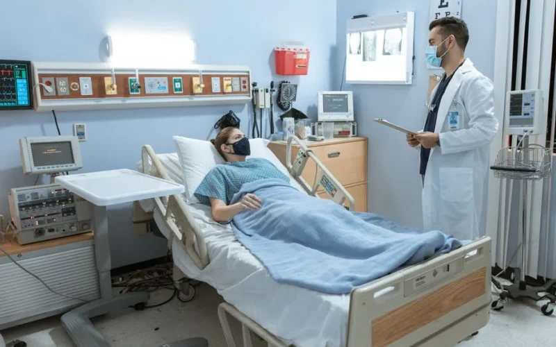 A doctor checking on a patient in a hospital room, both wearing face masks for safety.