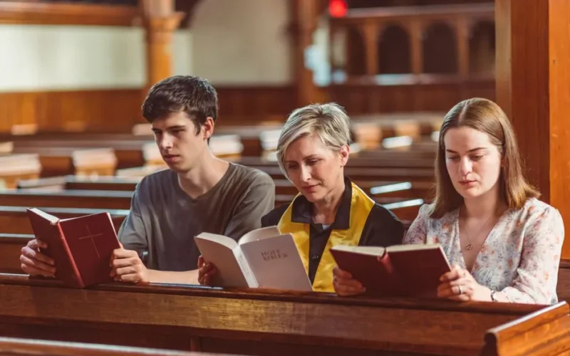 Three individuals reading bibles together in a church setting.
