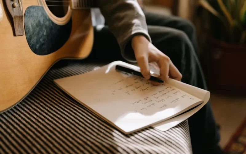 A person writing lyrics with an acoustic guitar, conveying creativity and musical inspiration.
