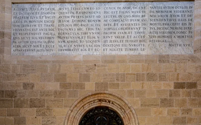 Close-up of a historic wall with Latin script above a circular window.