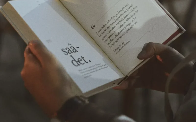 Person holding and reading an open book with visible text.