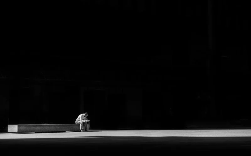 A lone man sitting on a bench, captured in striking black and white, conveying solitude and contemplation.