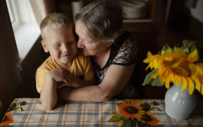 A loving embrace between grandmother and grandson at a sunlit table with sunflowers.
