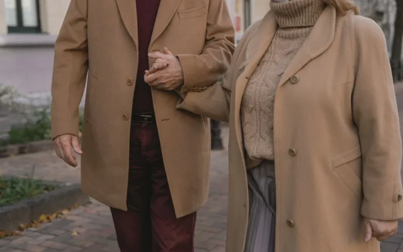 Senior couple holding hands while walking outside in autumn clothing, showcasing love and companionship.