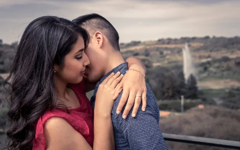 A loving couple embraces on an outdoor terrace overlooking scenic landscape.