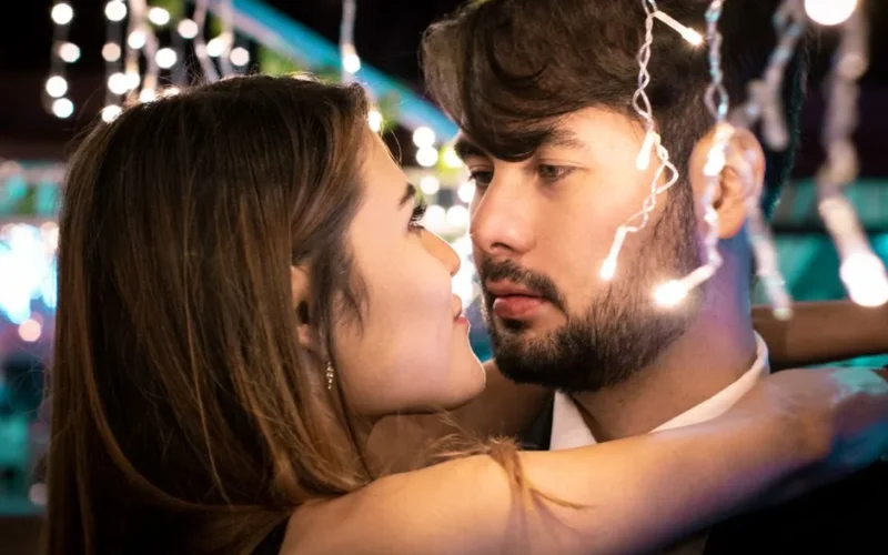Close-up of a young couple embracing and gazing at each other romantically under string lights.