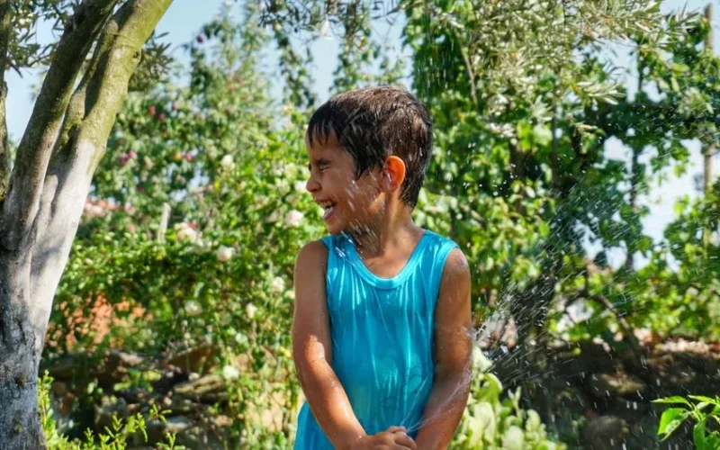 A cheerful child enjoys a refreshing splash of water in a sunny garden setting.