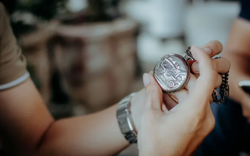 Detailed view of hands holding an antique pocket watch with chain outdoors.