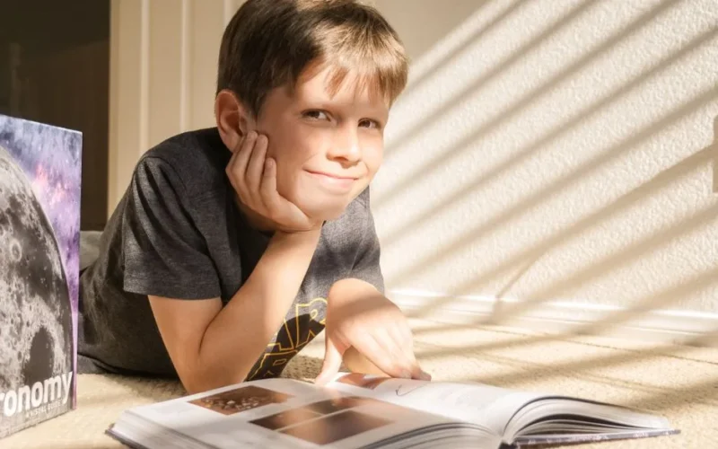 A curious child enjoys reading an astronomy book in a sunlit room.
