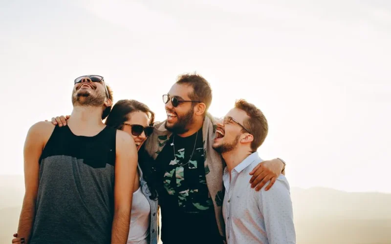 A group of young adults laughing and enjoying time together outdoors under the sun.