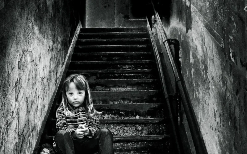 A girl sitting alone in the stairs with her doll looking sad and neglected