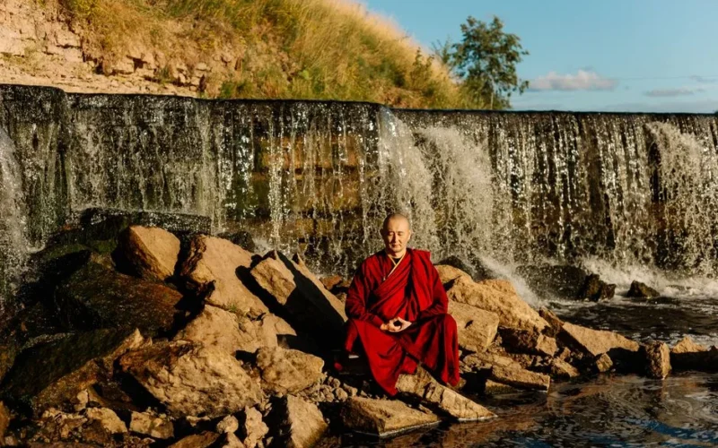 A Buddhist monk meditating peacefully by a waterfall, embracing tranquility in nature.