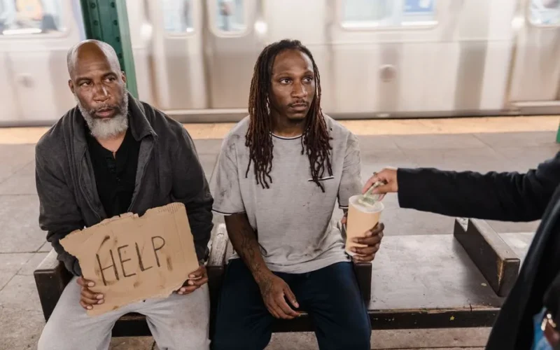 Two men in a subway station seeking help, with a passerby offering money.