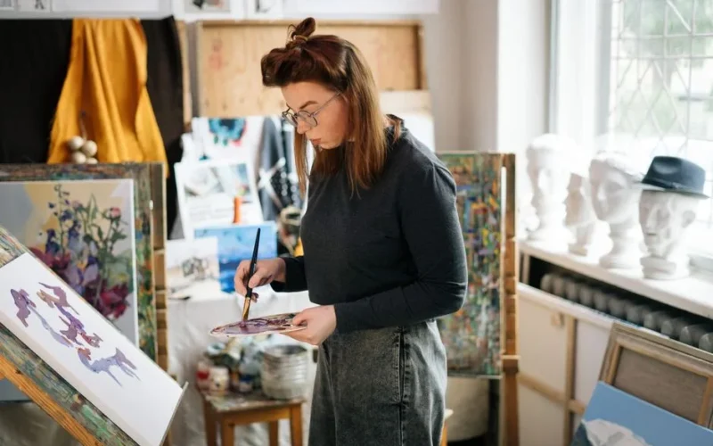 Woman artist painting on canvas in a bright, sunlit studio. Creative and focused atmosphere.