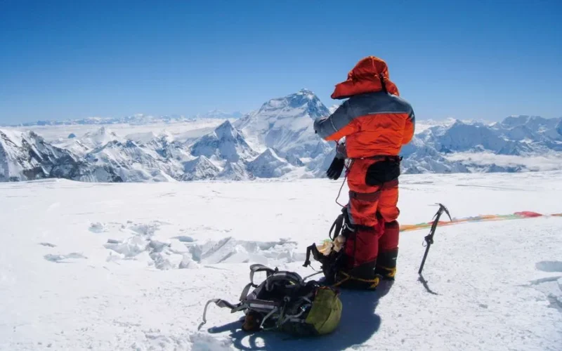 Mountaineer in puffer jacket on snowy peak in Nepal's Himalayas.