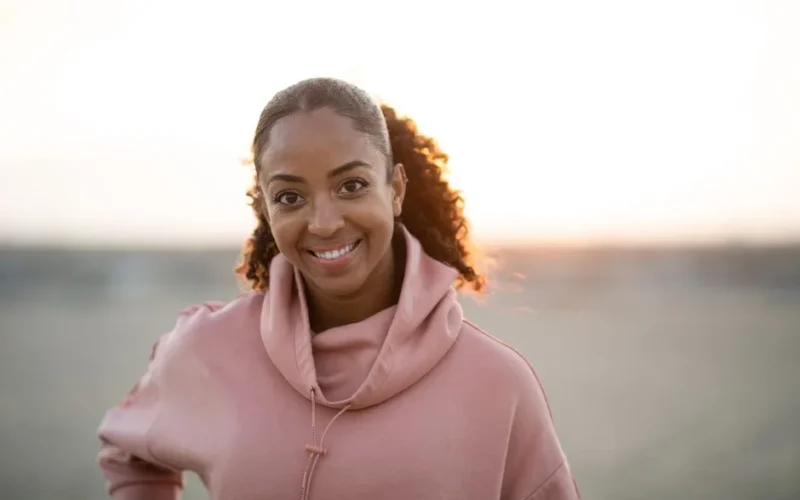Cheerful woman in a pink hoodie enjoys a sunrise outdoors, exuding warmth and positivity.