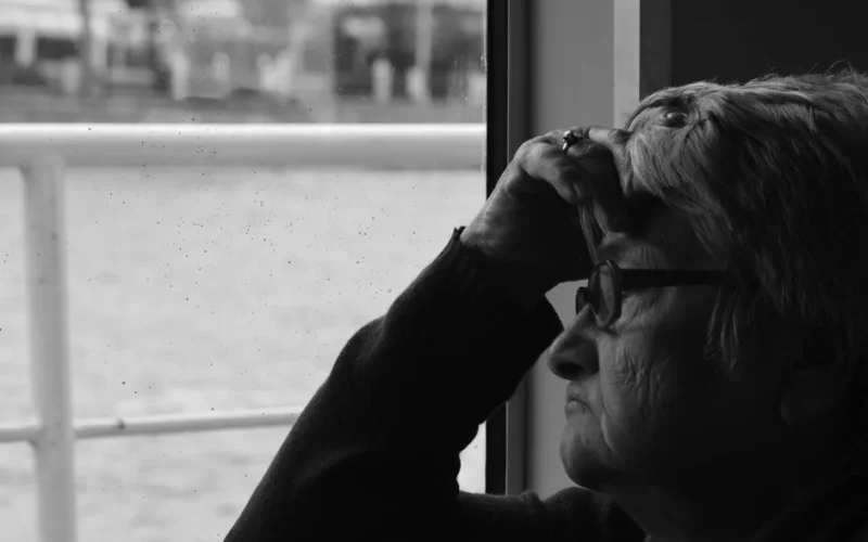Black and white portrait of a senior woman thoughtfully gazing out of a window.