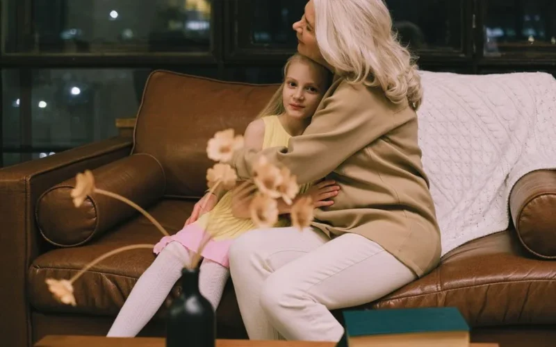 Grandmother and granddaughter hugging on a sofa, sharing a warm moment indoors.