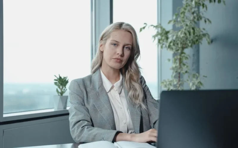 Professional businesswoman at a desk in a bright office with a laptop and notebook.