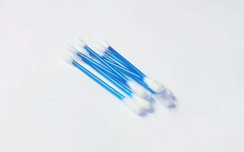 A minimalistic close-up image of blue handled cotton swabs on a white surface.